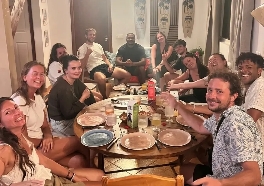 Voyageurs souriants autour de la grande table ronde de la salle commune, le soir