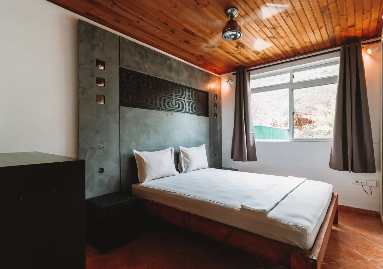 Chambre double : grand lit blanc, tête de lit en béton ciré