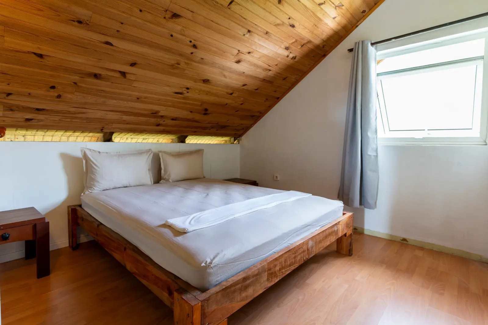 Chambre double à l'étage : lit double en bois sous le plafond lambrissé en pente